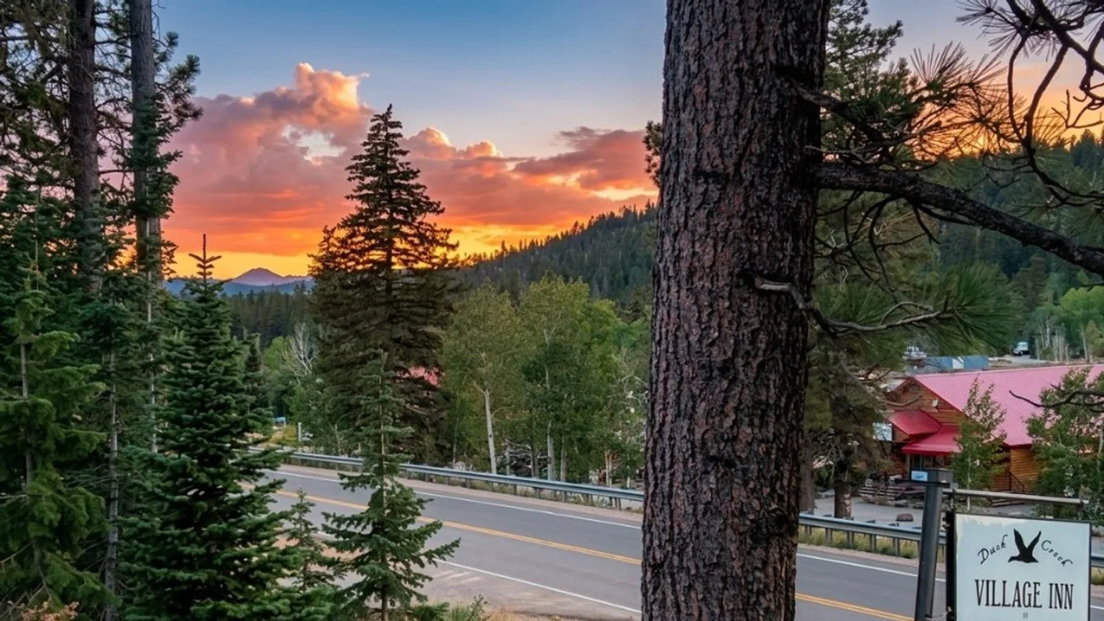 Highway 14 curving past the Duck Creek Village Inn sign at sunset, with pines and an orange sky over Cedar Mountain