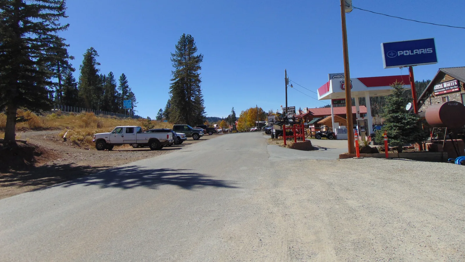 Movie Ranch Road running west through Duck Creek Village, Utah, past the fuel pumps and pines under a clear autumn sky