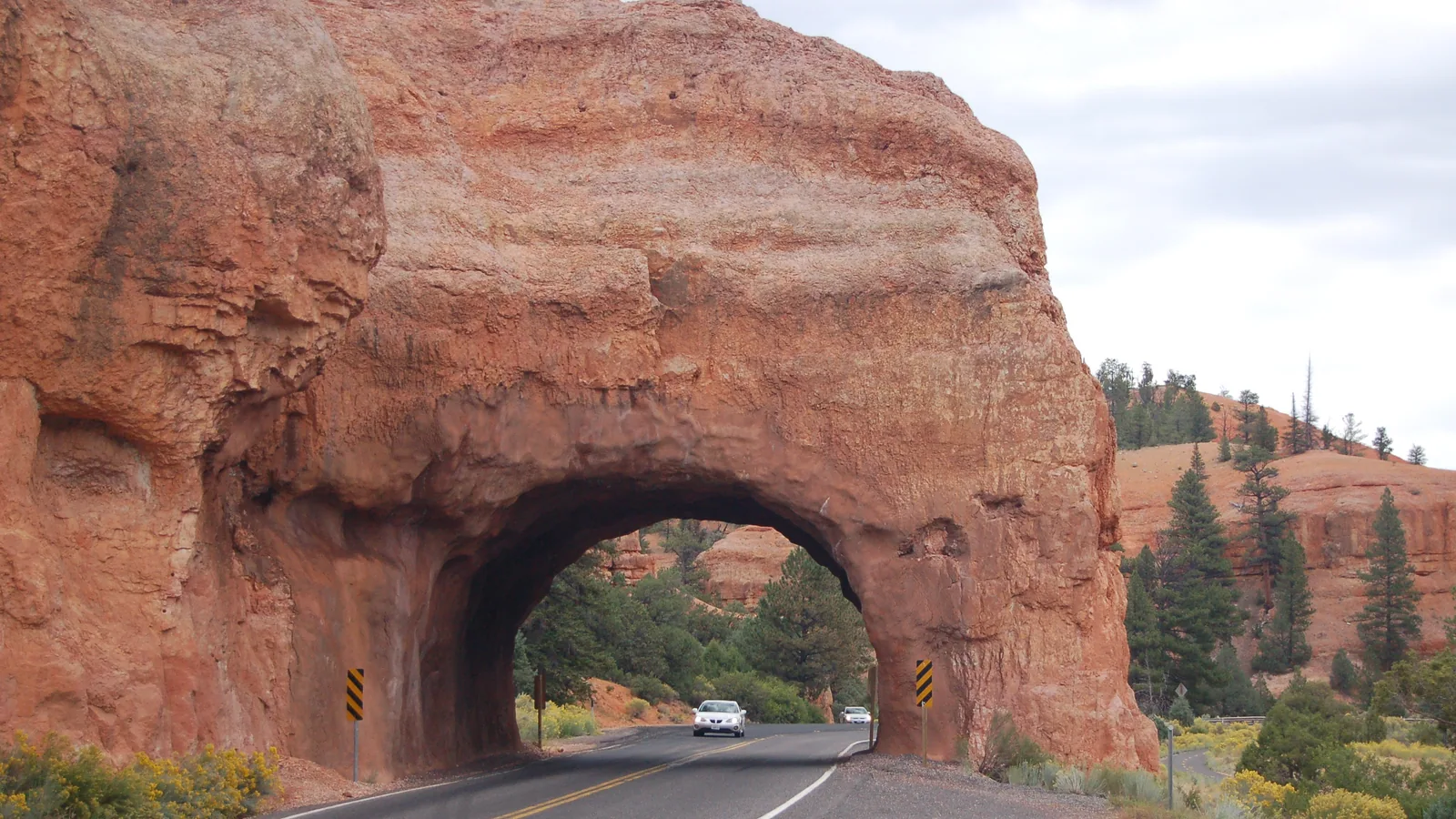Scenic Byway 12 door een oranje rotstunnel in Red Canyon, Dixie National Forest, met ponderosa dennen op de achtergrond